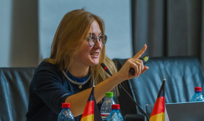 Speaker at a conference table with German flags